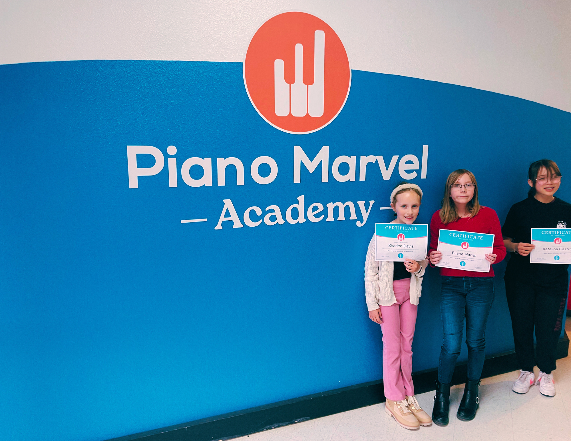 5 Three piano students holding certificates in front of the Piano Marvel Academy wall in Lubbock, TX